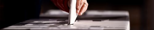 A person is putting a paper into a voting box.